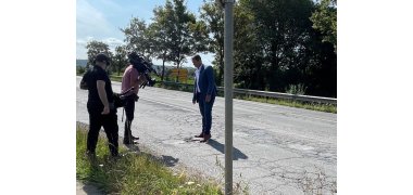 Auf der Straße steht Bürgermeister Przybylla und zeigt dem links stehenden Drehteam die Schlaglöcher. 