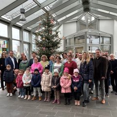 Vor dem Weihnachtsbaum stehen die Kinder der Kita St. Raphael, Erzieherin Ulrike Dinnebier, Erzieher Dirk Butz mit Gitarre, Bürgermeister Thomas Przybylla und Mitarbeiterinnen und Mitarbeiter des VG-Rathauses. 