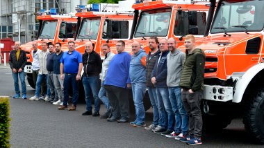 Direkt vor den neuen Mehrzweckfahrzeugen stehen Mitglieder der Feuerwehreinheiten. Von den Fahrzeugen ist jeweils nur das Fahrerhaus und die Motorhaube zu sehen. 