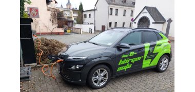 Das Bürgerauto steht rechts, links ist die Ladesäule zu sehen und das Kabel ,das von der Säule zu dem Auto führt. 