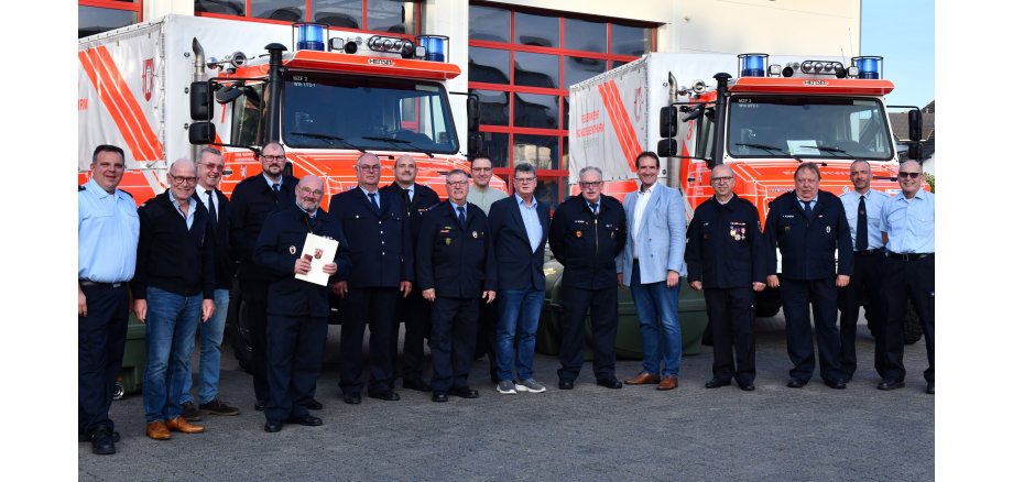 Vor zwei Feuerwehrfahrzeugen stehen die Geehrten mit dem Bürgermeister der Verbandsgemeinde, Thomas Przybylla, Wehrleiter Arnd Lenarz und weiteren Ehrengästen. 