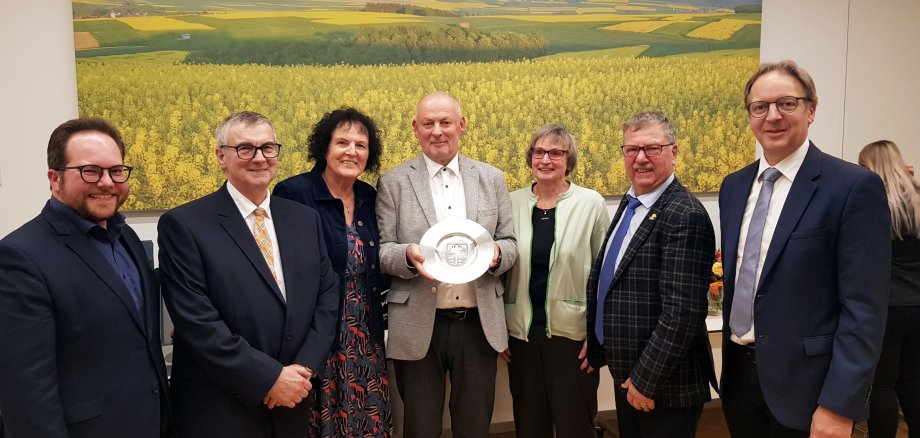 Willibald Görg steht mit dem Wappenteller in der Hand neben seiner Frau, dem Landrat Dr. Alexander Saftig und weiteren Gratulanten.